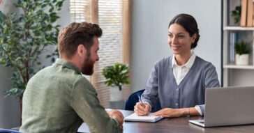 Female counsellor behind desk taking notes with male client